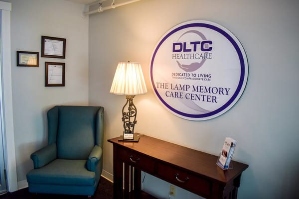 Cozy lobby with a blue armchair, lamp, and signage for The Lamp Memory Care Center.