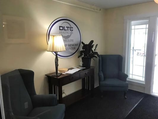 Cozy lobby with two chairs, a lamp, a plant, and a sign