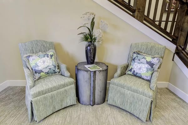 Two green chairs with floral pillows beside a small table