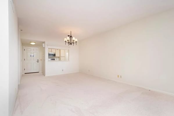 Empty living room with chandelier and kitchen view