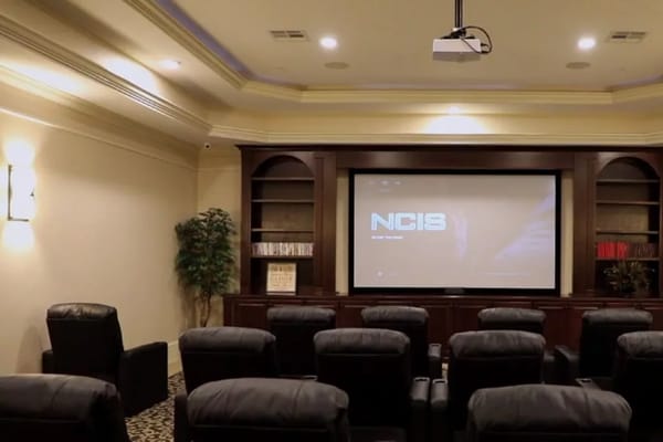 Comfortable seating in a theater room with a large screen displaying NCIS.