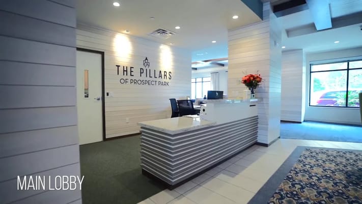 Welcoming lobby of The Pillars of Prospect Park with a reception desk and floral arrangement.