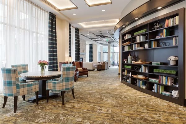 Lounge area with chairs, a table, and a bookshelf in a senior living facility.