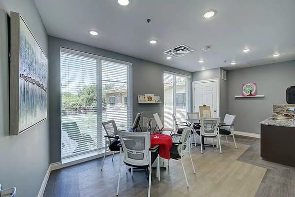 Bright activity room with tables and chairs, featuring large windows