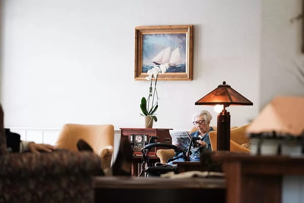 An elderly resident reading a newspaper in a cozy living room.