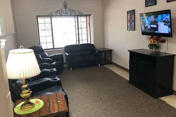 A cozy living room with black leather sofas, a lamp, and a television.