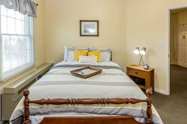 Well-decorated bedroom with a bed, nightstand, and natural light.