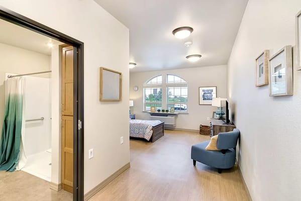 A well-lit bedroom featuring a bed, chair, and window with a scenic view.