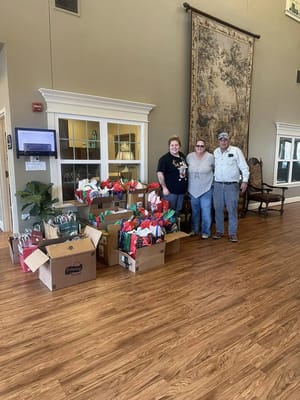 Three staff members pose next to a pile of holiday gifts in the lobby.