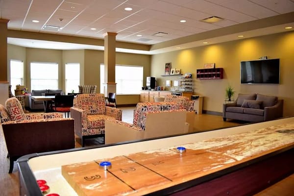 Spacious common area featuring comfortable seating and a shuffleboard table.