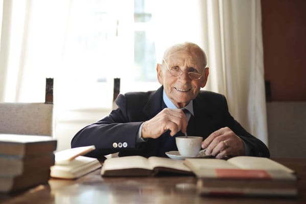 An elderly man enjoying coffee at a table with books