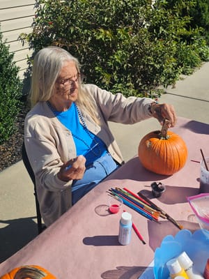 Resident painting a pumpkin at an outdoor table