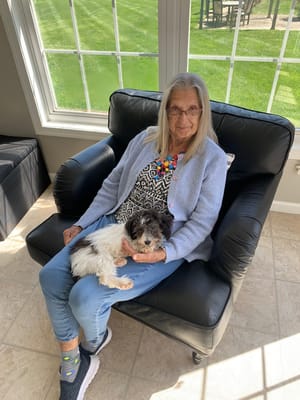 An elderly woman sitting with a small dog in a sunlit room