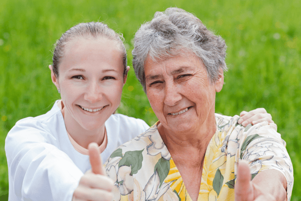A staff member and a resident giving thumbs up outdoors.