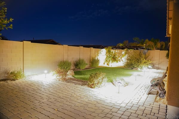 Illuminated backyard with grass and plants at night.