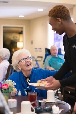 Staff serving food to a smiling resident in the dining area