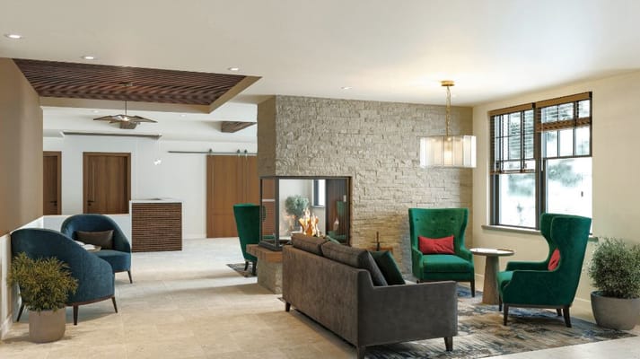 Lounge area with green chairs, a gray sofa, and a stone fireplace.