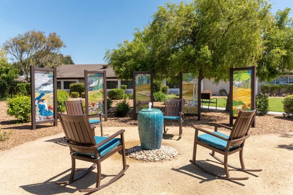 Rocking chairs surrounding a blue water feature and art panels in a garden setting.