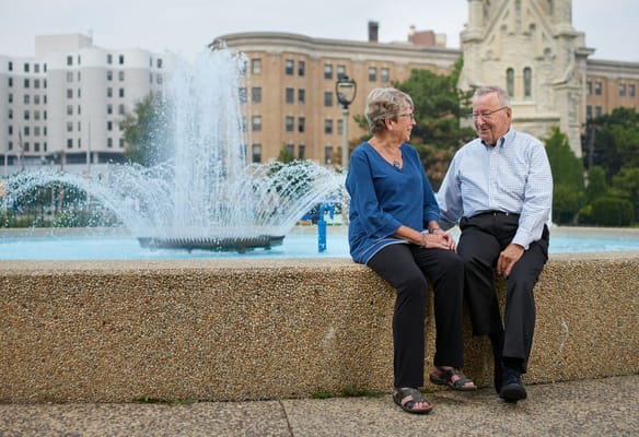 Two seniors engaged in conversation near a fountain.