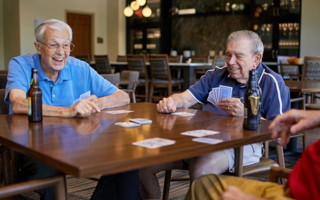 Two elderly men playing cards at a table with drinks