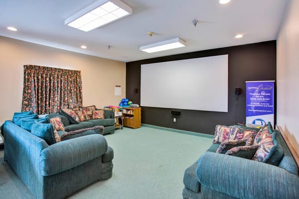 Comfortable seating in a recreation room with a large screen and floral curtains.