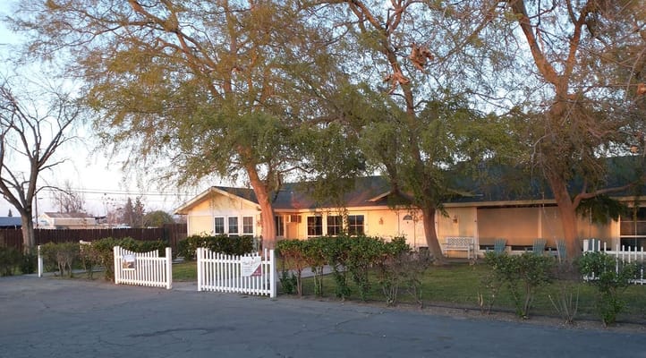 Front view of Redwood Senior Living with a white fence and trees.