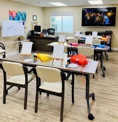 An activity room set up for a painting session with easels, paints, and supplies.