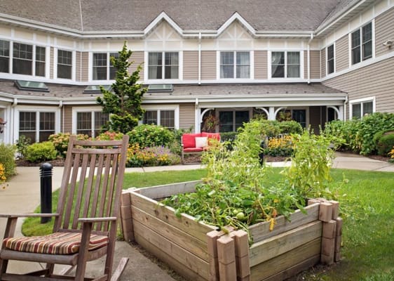 Raised garden bed with plants and a rocking chair in a landscaped courtyard.