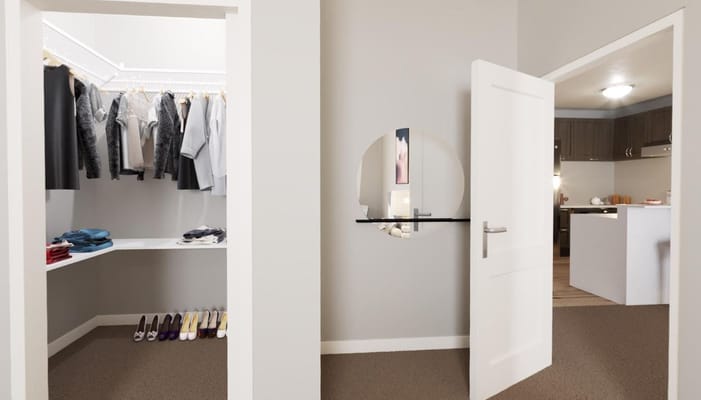 View of a modern closet with clothing and shoes, adjacent to a kitchen.