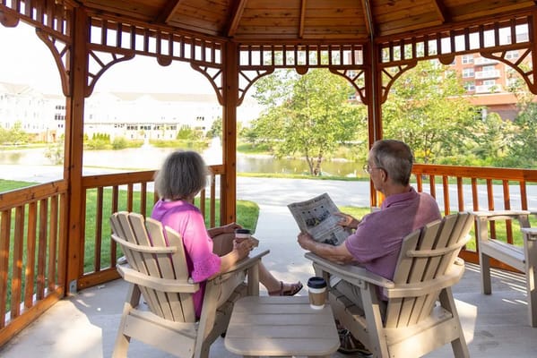 Two residents sitting in a gazebo, one reading a newspaper and the other enjoying a beverage.