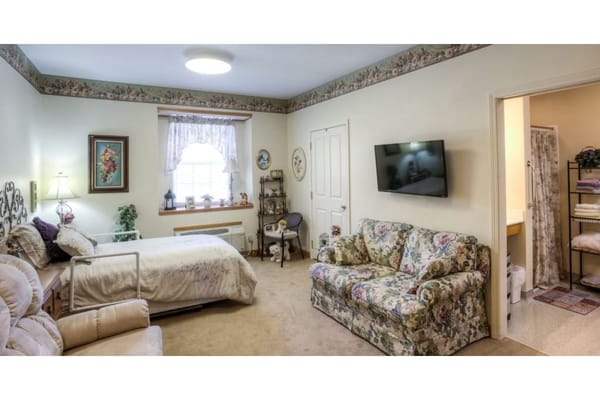 A cozy bedroom featuring a bed, comfy armchair, and a floral couch.