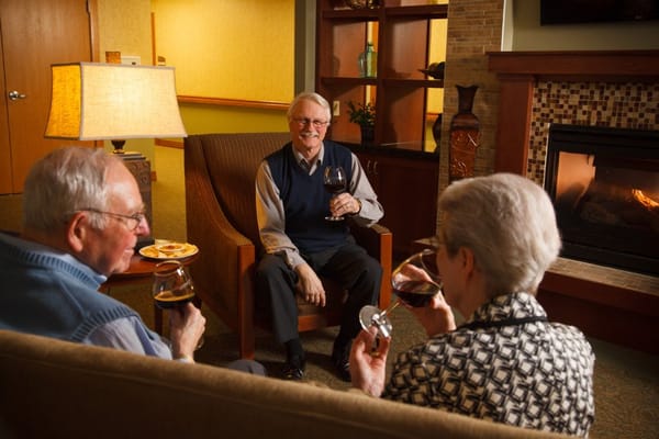 Three residents toast with glasses of red wine in a cozy living area.