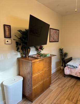 A tidy bedroom with a dresser, a flat-screen TV, and a small bed adorned with a floral quilt.