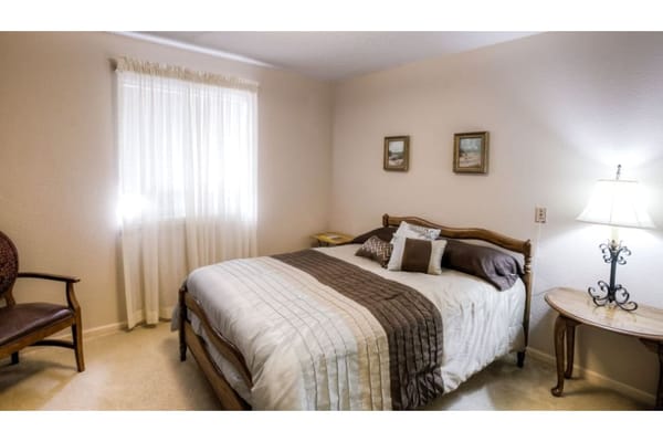A cozy bedroom with a neatly made bed, two windows with curtains, and decorative items on the walls.