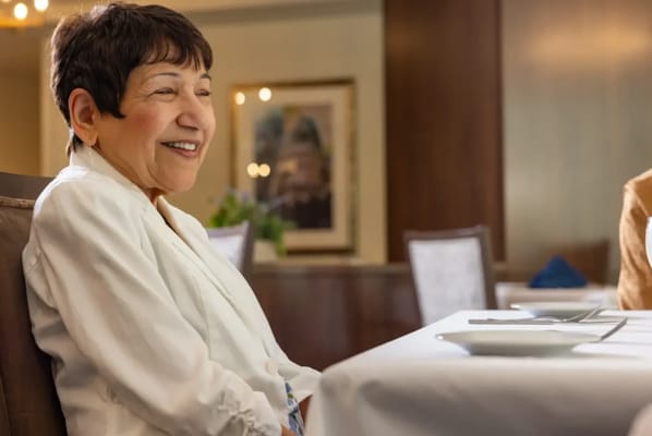 A smiling woman seated at a dining table in a facility