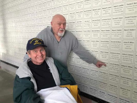 Two residents near a wall of name plaques