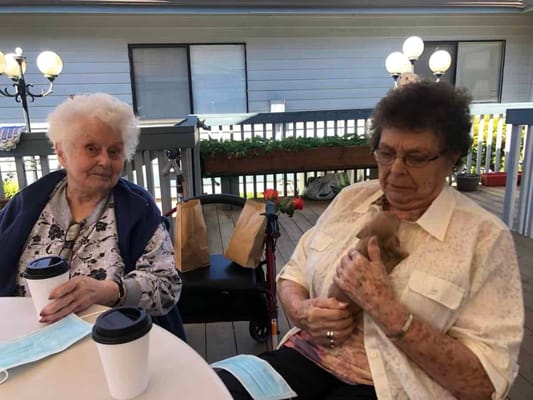 Two residents enjoying coffee and a puppy outdoors