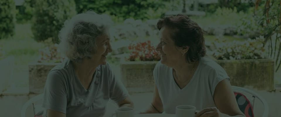 Two elderly women enjoying coffee in a garden setting
