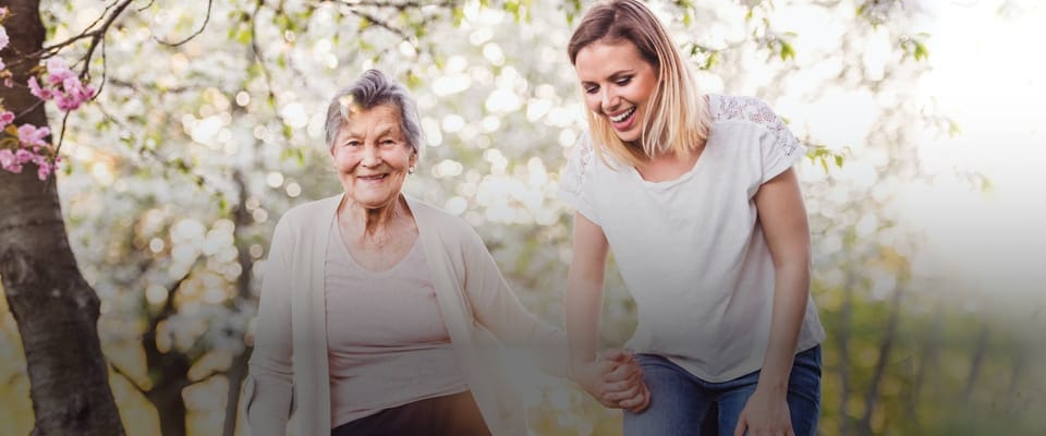An elderly woman walking outside with a caregiver