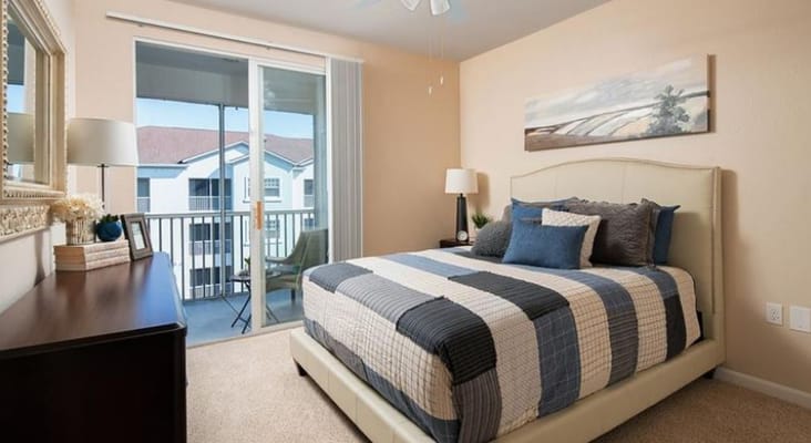 Bright bedroom with a bed, dresser, and balcony view.
