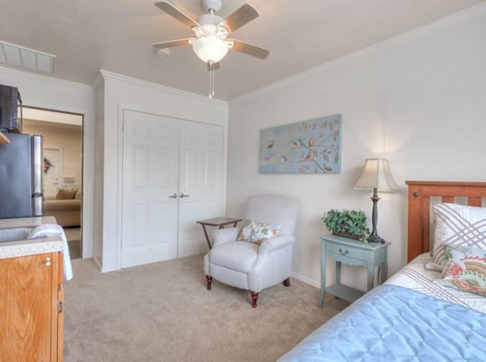 A cozy bedroom featuring a chair, side table, and bed with colorful bedding.