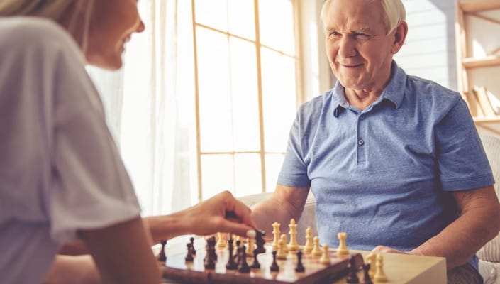An elderly man smiling while playing chess with a younger woman