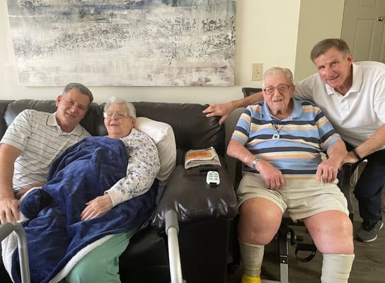 Two seniors and two family members enjoying time together on a couch.