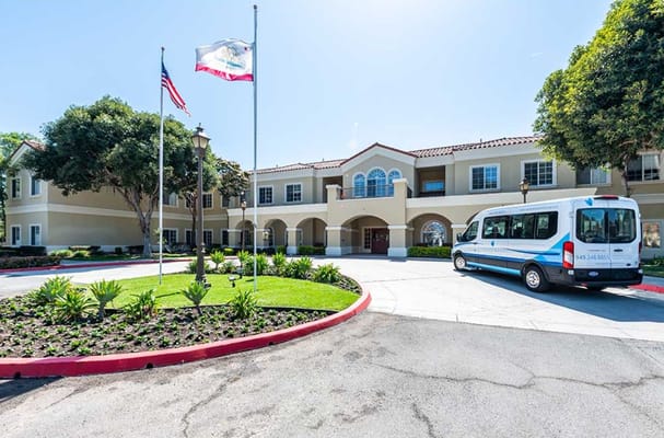 Exterior view of Capistrano Senior Living with flags and shuttle van