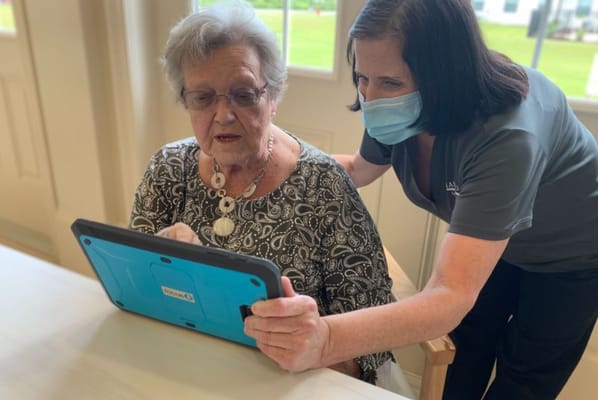 Staff assisting a resident with a tablet in a communal area