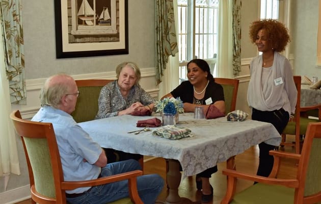 Two residents and two staff members engaged in conversation at a dining table.