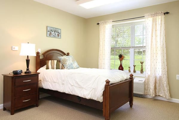 A well-lit bedroom featuring a wooden bed, bedside table, and curtains.