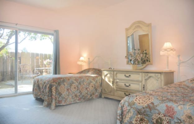 A cozy bedroom with two beds and a dresser, opening to an outdoor patio.