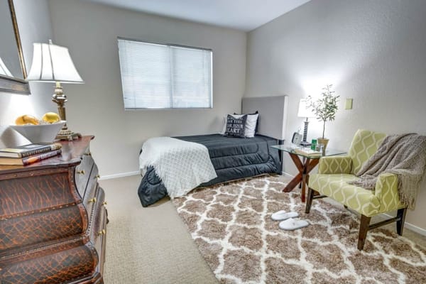 A well-furnished bedroom with a bed, armchair, and lamp.