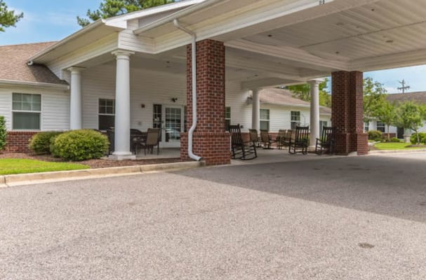 A covered entrance with rocking chairs and landscaping at Spring Oak Conway.